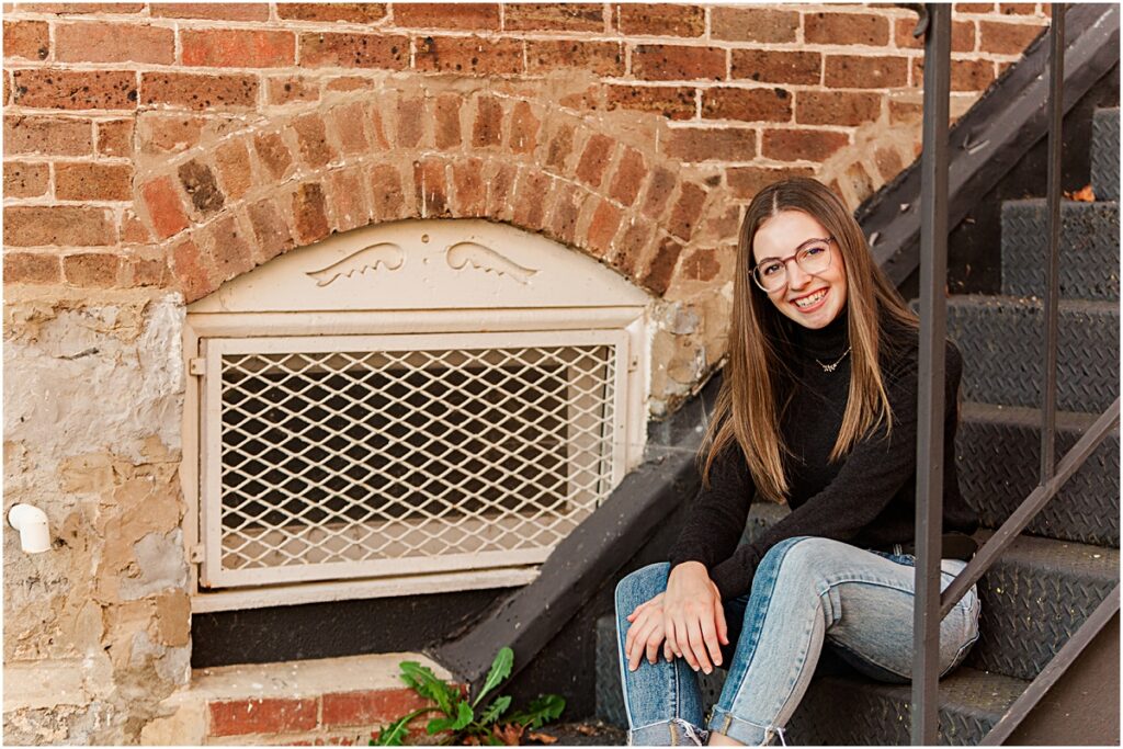 Senior client sitting on stairs in front of brick building during Senior Pictures session in VA