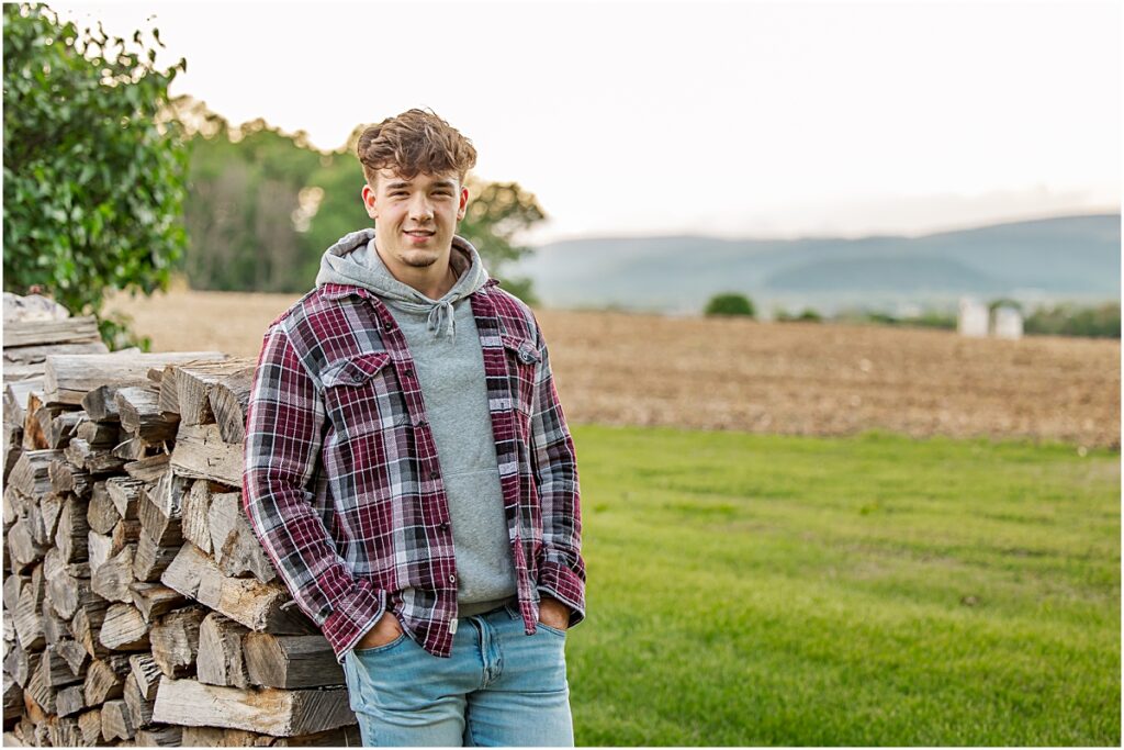 A graduate posing against a wood pile in a field to show how to accessorize according to these senior photography tips. 