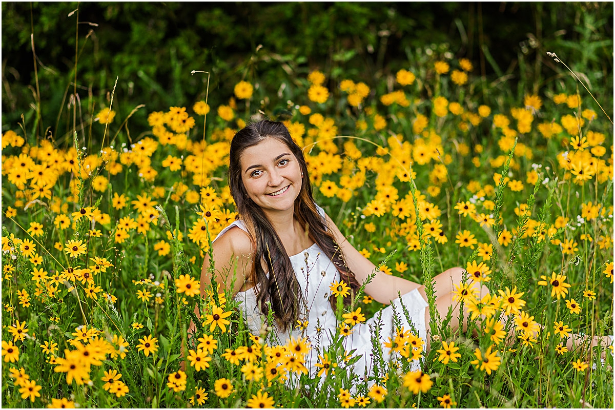 Graduate sitting in a field of yellow flowers, showing off her outfit to illustrate some senior photography tips.