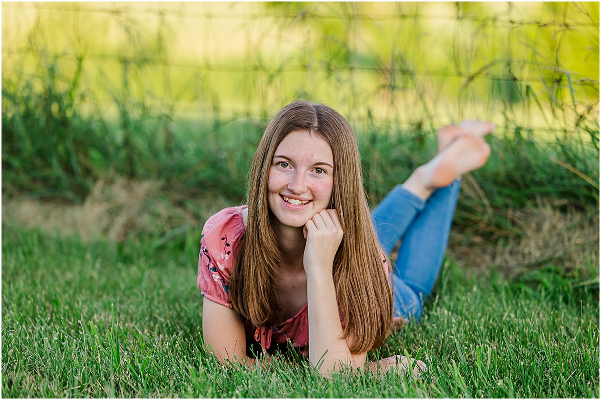 Jerica laying on the grass in front of an old fence;  photos done by a Virginia senior photographer